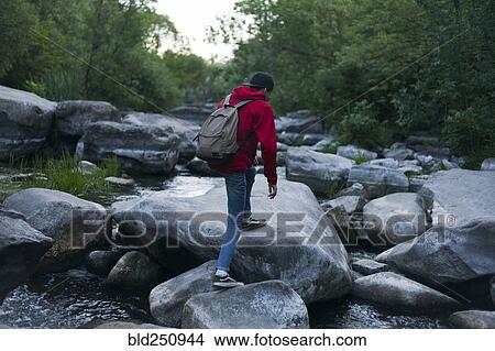 Picture - Caucasian man hiking on rocks in river. Fotosearch