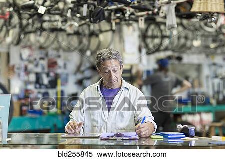 Stock Photography - Caucasian man in bicycle shop writing on clipboard. Fotosearch