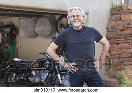 Stock Photo - Caucasian man in driveway with motorcycle. Fotosearch