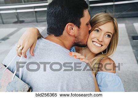 Stock Photography - Caucasian man kissing cheek of woman carrying shopping bag. Fotosearch
