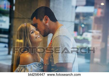 Stock Photo - Caucasian man kissing woman on cheek behind window. Fotosearch