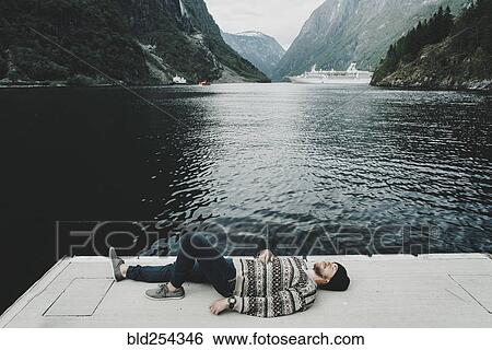 Stock Photograph - Caucasian man laying on dock at waterfront. Fotosearch