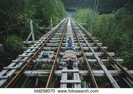 Stock Image - Caucasian man laying on train tracks. Fotosearch