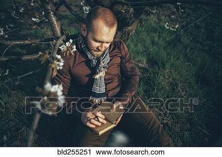 Caucasian man leaning on tree writing in journal View Large Photo Image Stock Image - Caucasian man leaning on tree writing in journal. Fotosearch