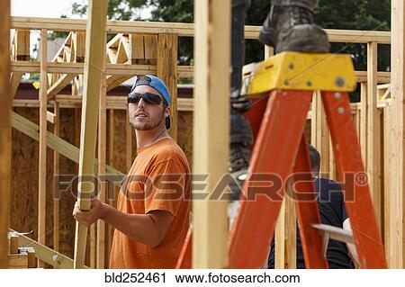 Stock Image - Caucasian man lifting lumber at construction site. Fotosearch