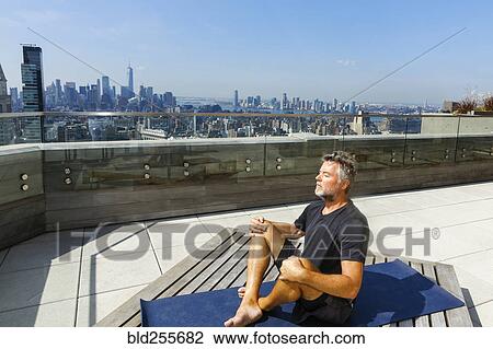 Stock Image - Caucasian man meditating on urban rooftop. Fotosearch