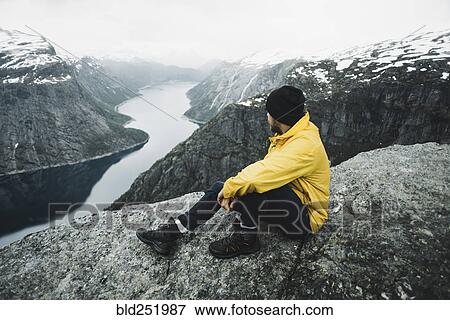 Stock Photo - Caucasian man on cliff admiring scenic view of mountain river. Fotosearch