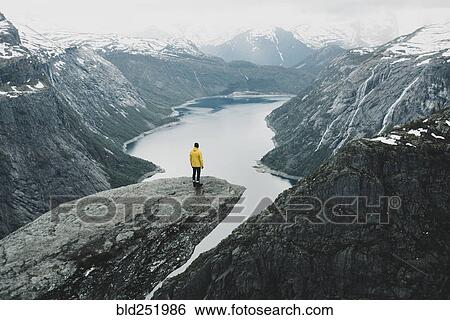 Stock Photograph - Caucasian man on cliff admiring scenic view of mountain river. Fotosearch