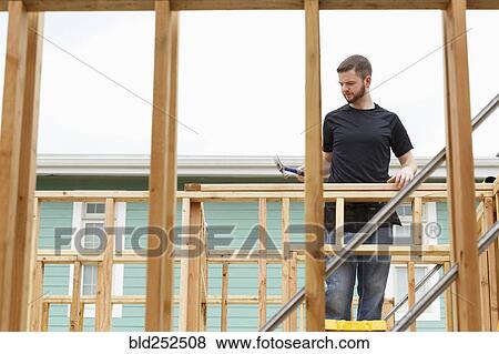 Stock Photo - Caucasian man on ladder using hammer at construction site. Fotosearch