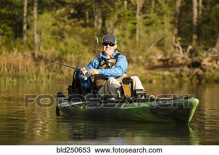 Stock Image - Caucasian man pedaling in kayak and fishing. Fotosearch