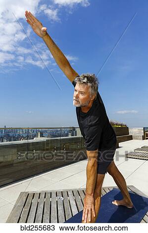Stock Image - Caucasian man performing yoga on urban rooftop. Fotosearch