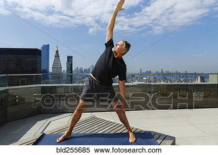 Stock Photography - Caucasian man performing yoga on urban rooftop. Fotosearch