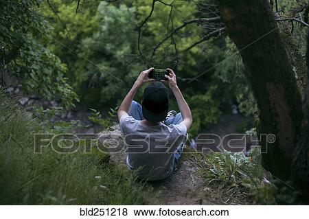 Stock Photo - Caucasian man photographing with cell phone in woods. Fotosearch