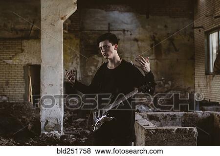 Stock Photo - Caucasian man playing guitar in rubble. Fotosearch