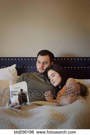 Stock Photo - Caucasian man reading book in bed cuddling with woman. Fotosearch