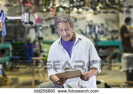 Stock Image - Caucasian man reading clipboard in bicycle shop. Fotosearch