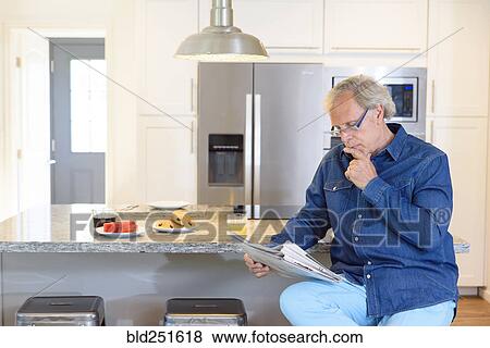 Stock Photo - Caucasian man reading newspaper in kitchen. Fotosearch