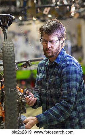 Stock Photo - Caucasian man repairing bicycle in shop. Fotosearch