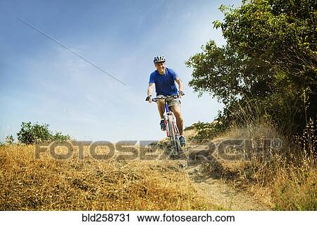 Stock Image - Caucasian man riding bicycle on path. Fotosearch