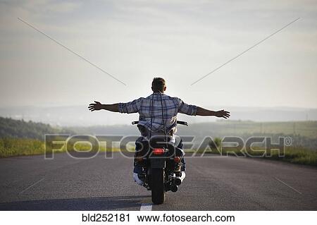 Stock Image - Caucasian man riding motorcycle with arms outstretched. Fotosearch