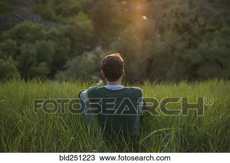 Stock Image - Caucasian man sitting in grass. Fotosearch