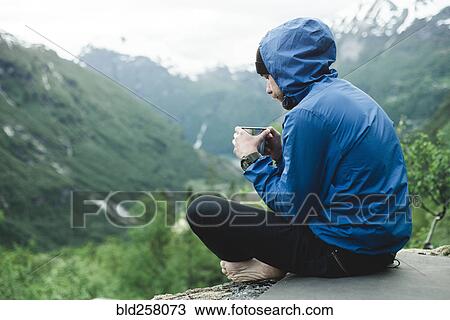 Stock Image - Caucasian man sitting in mountain landscape drinking coffee. Fotosearch
