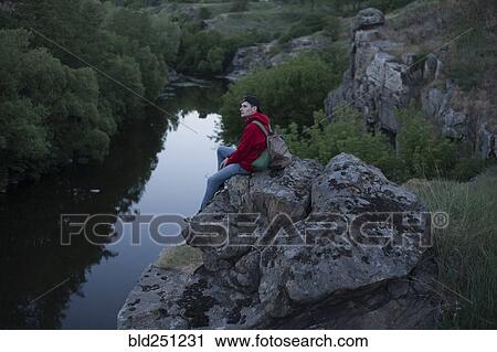 Stock Image - Caucasian man sitting on a rock near river. Fotosearch