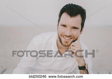 Stock Photograph - Caucasian man sitting on beach. Fotosearch