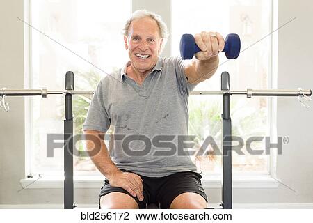 Stock Image - Caucasian man sitting on bench lifting dumbbell. Fotosearch
