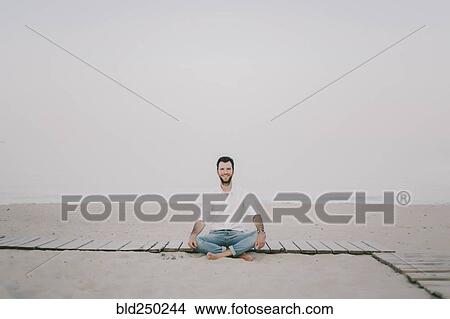 Picture - Caucasian man sitting on boardwalk at beach. Fotosearch