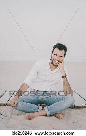 Stock Photography - Caucasian man sitting on boardwalk at beach. Fotosearch