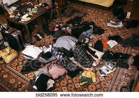 Stock Photography - Caucasian man sitting on messy floor with shirt covering head. Fotosearch