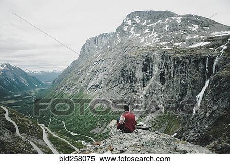 Stock Photography - Caucasian man sitting on rock admiring scenic view of valley. Fotosearch