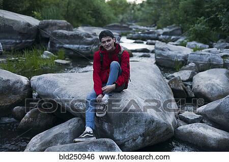 Stock Photograph - Caucasian man sitting on rock in river. Fotosearch