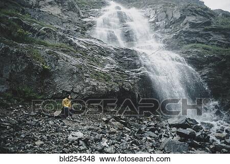 Caucasian man sitting on rock watching waterfall View Large Photo Image Stock Photo - Caucasian man sitting on rock watching waterfall. Fotosearch