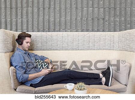 Caucasian man sitting on sofa wearing headphones texting on cell phone View Large Photo Image Stock Image - Caucasian man sitting on sofa wearing headphones texting on cell phone. Fotosearch