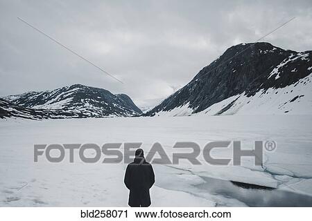 Stock Image - Caucasian man standing in mountain landscape in winter. Fotosearch