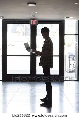 Caucasian man standing near doorway using laptop View Large Photo Image Stock Image - Caucasian man standing near doorway using laptop. Fotosearch