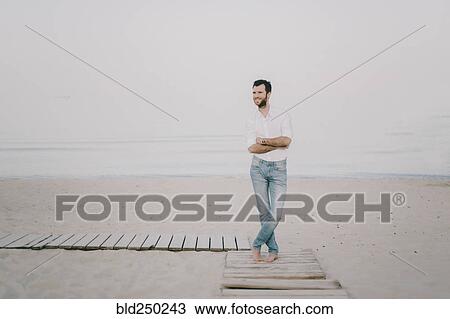 Stock Image - Caucasian man standing on boardwalk at beach. Fotosearch