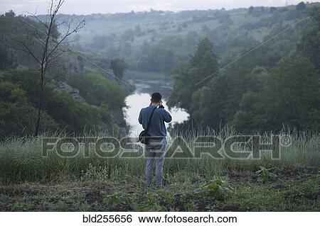 Caucasian man standing on hill photographing river View Large Photo Image Stock Photograph - Caucasian man standing on hill photographing river. Fotosearch
