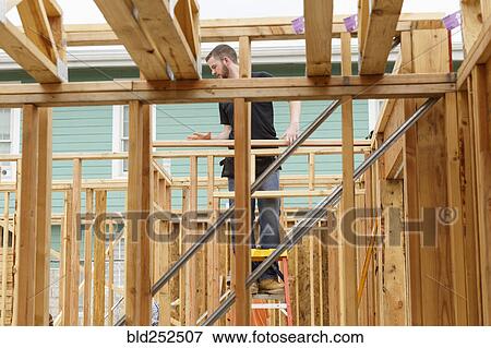 Stock Photo - Caucasian man standing on ladder at construction site. Fotosearch
