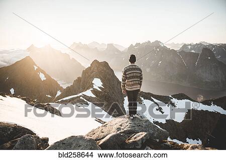 Picture - Caucasian man standing on rock admiring scenic view of mountain lake. Fotosearch