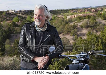 Stock Image - Caucasian man standing with motorcycle. Fotosearch