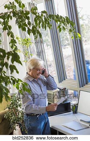 Stock Photograph - Caucasian man talking on cell phone and reading notebook. Fotosearch
