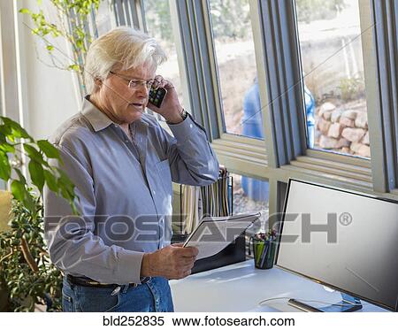 Stock Photography - Caucasian man talking on cell phone and reading notebook. Fotosearch