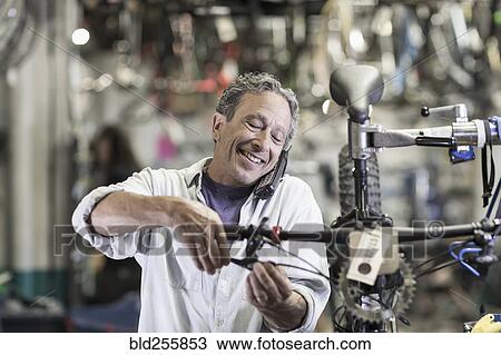 Stock Image - Caucasian man talking on telephone and repairing brakes on bicycle. Fotosearch