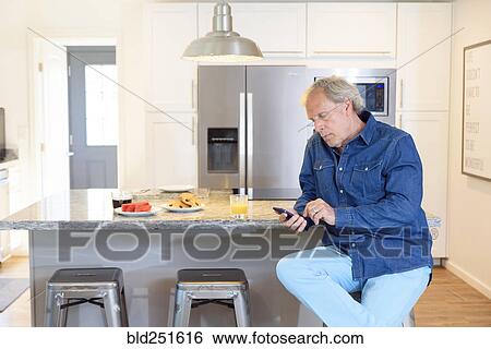 Caucasian man texting on cell phone in the kitchen View Large Photo Image Stock Photograph - Caucasian man texting on cell phone in the kitchen. Fotosearch