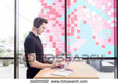 Stock Image - Caucasian man typing on laptop and listening to headphones. Fotosearch