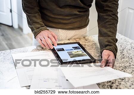Stock Photo - Caucasian man using digital tablet and holding paperwork. Fotosearch