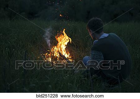 Stock Photo - Caucasian man with campfire at night. Fotosearch
